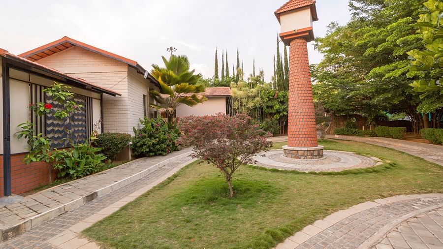 Lush garden with pathway and central pillar near cottages at Nirantara Resort & Spa