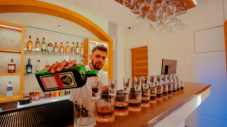 A bartender prepares drinks at a well-stocked bar at Nirantara Resort & Spa, showcasing a variety of liquors and glassware.