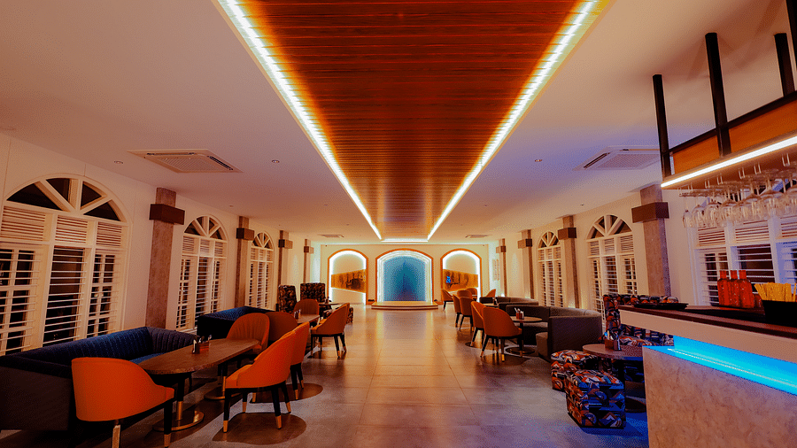 A long, brightly lit hallway with a bar area on the right, featuring colourful lighting and a modern design -  Nirantara Resort & Spa