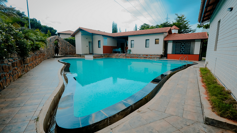 A uniquely shaped swimming pool at Nirantara Resort & Spa, Bengaluru, surrounded by plants and buildings.