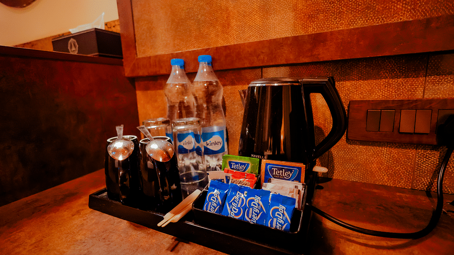 A close-up of a tray with a kettle, bottled water, and small snacks in a dimly lit setting  - Nirantara Resort & Spa.