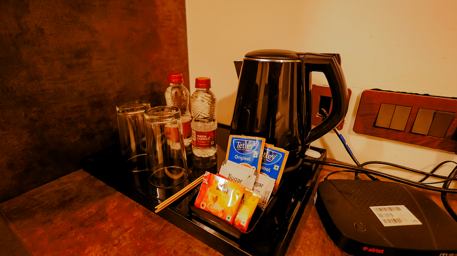 Close-up of amenities on a desk in a room at Nirantara Resort & Spa, Bengaluru, including a kettle, coffee, and a phone.