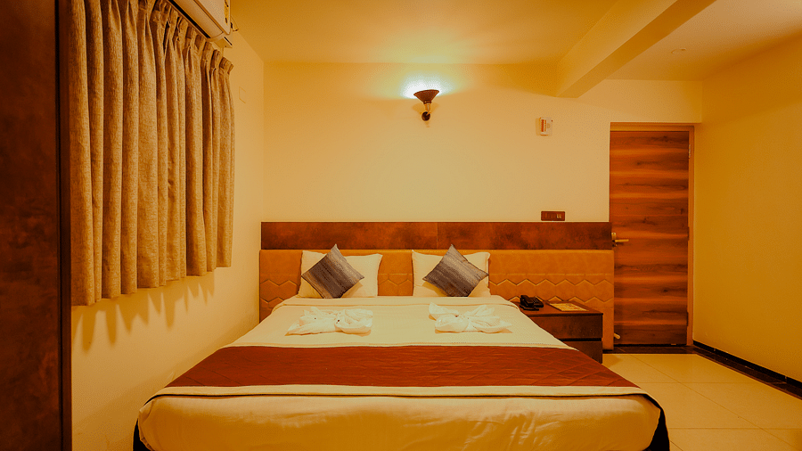 A comfortable bed in a room at Nirantara Resort & Spa, Bengaluru, with warm lighting and wooden furniture.