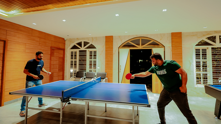 Two people playing table tennis in a well-lit room with large windows at Nirantara Resort & Spa.