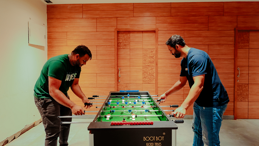 Two people playing foosball at Nirantara Resort & Spa in a room with wood-panelled walls.