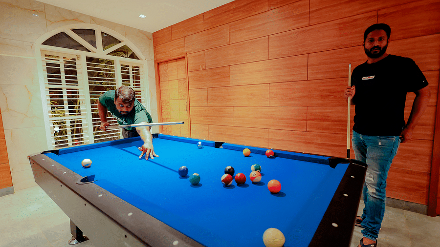 A person plays pool on a blue pool table in a room with brick walls and large windows - Nirantara Resort & Spa.