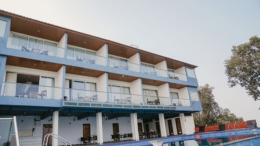 A facade image of the Nisarga Lake Resort with the swimming pool in the front surrounded by greenery