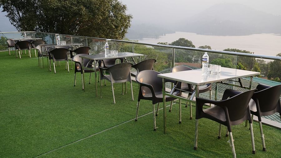 An image of the Lake View Oasis restaurant with chairs and tables at the rooftop and mountains and lake view in the background - Nisarga Lake Resort