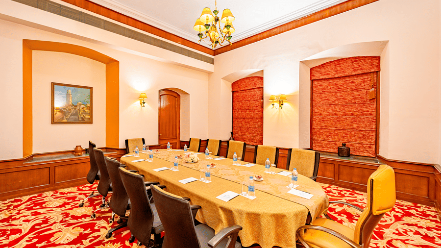 A wide-angle shot of the boardroom with regal interiors and a red floral carpet flooring, featuring a rounded conference table in the middle of the boardroom at Noor-Us-Sabah Palace, Bhopal.