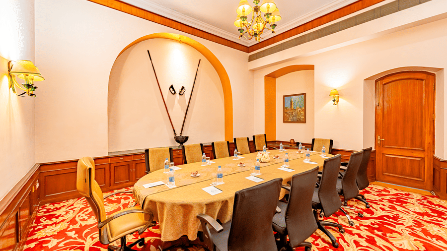 A brightly lit boardroom at the Noor-Us-Sabah Palace, Bhopal, featuring a conference table covered with an ochre yellow table cloth.