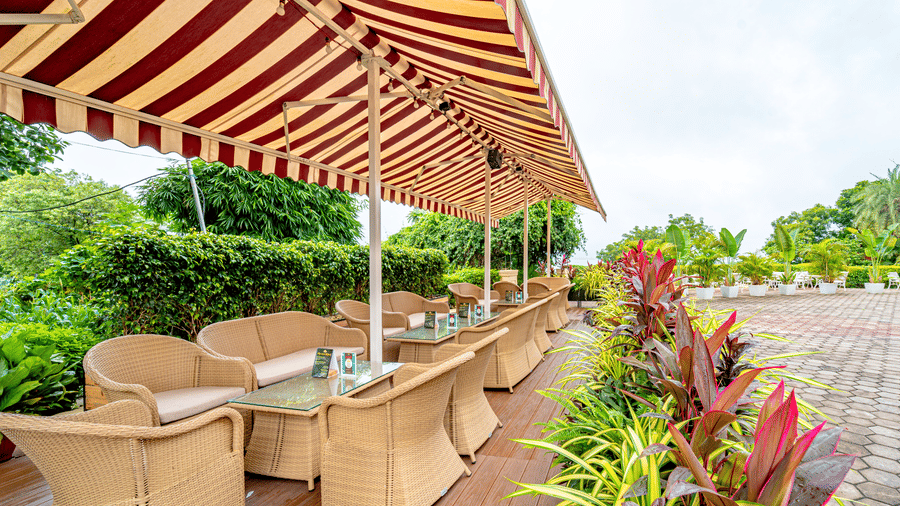 Outdoor seating area of Café Latte at Noor-Us-Sabah Palace, Bhopal, showing wicker chairs and tables under a striped awning with garden views.