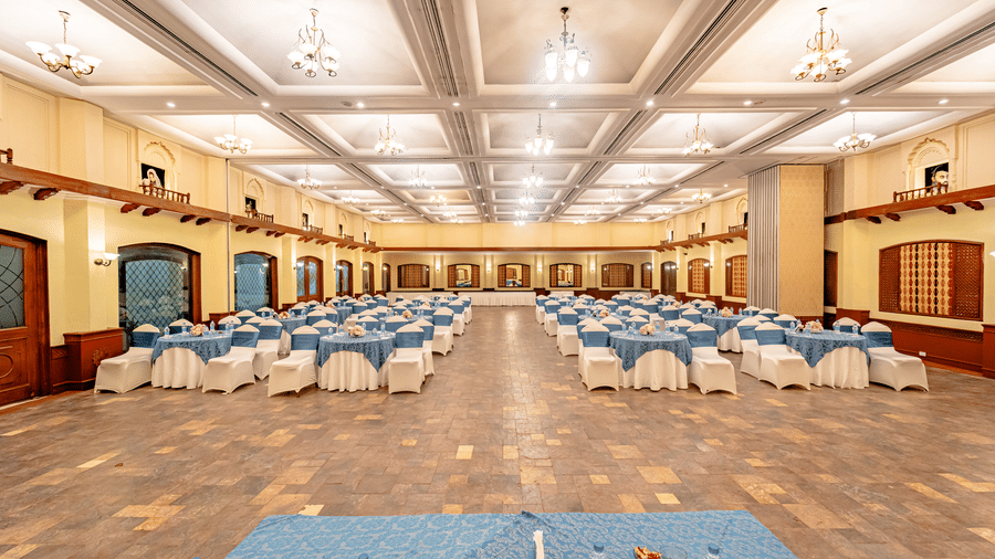 A panoramic shot of the Emperor Hall at Noor-Us-Sabah Palace, Bhopal, with grey tile flooring, featuring the tables and chairs arranged in a round-table seating arrangement.