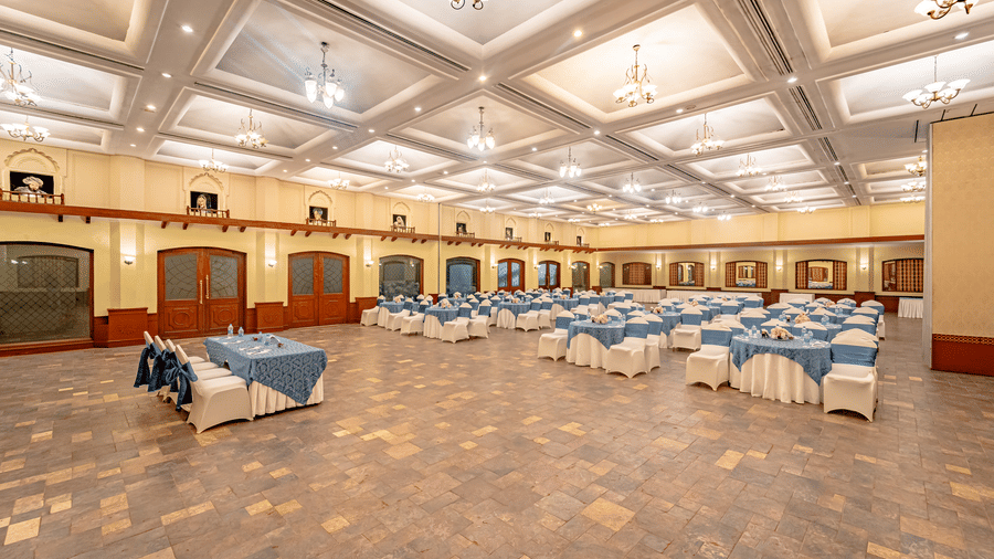 A wide-angle shot of the expansive Emperor Hall at Noor-Us-Sabah Palace, Bhopal, showcasing the tables and chairs arranged in a round table seating configuration.