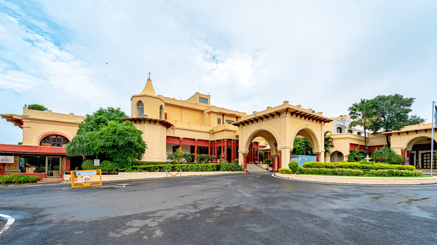 The grand front facade of Noor-Us-Sabah Palace, Bhopal, showing the arched main entrance, circular driveway, and lush green landscaping.
