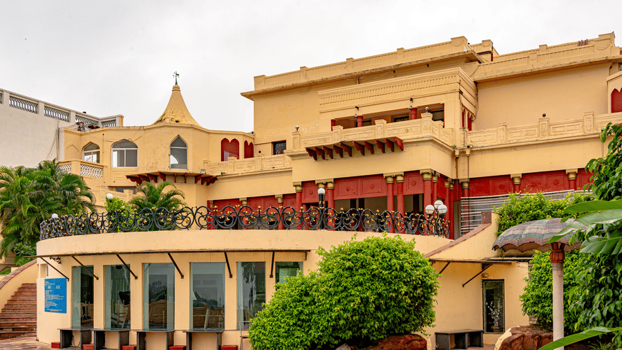 The rear facade of Noor-Us-Sabah Palace, Bhopal, featuring a curved terrace, sandstone architecture, and a glimpse of the swimming pool area.