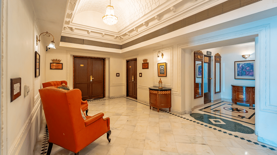 A wide-angle shot of the corridor leading to the elevator at Noor-Us-Sabah Palace, Bhopal, with 2 arm chairs.