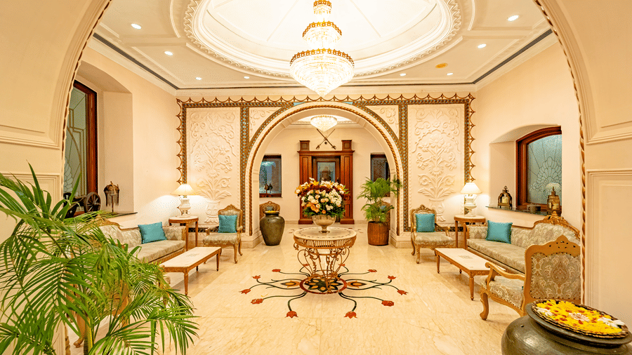 The expansive brightly lit lobby area at Noor-Us-Sabah Palace, Bhopal, featuring elegant seating arrangements along with a beautiful chandelier hanging from the ceiling.