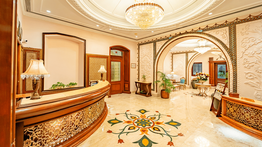 A wide-angle shot of the lobby of Noor-Us-Sabah Palace, Bhopal, featuring the reception desk in the corner overlooking the seating area through the arched hallway.