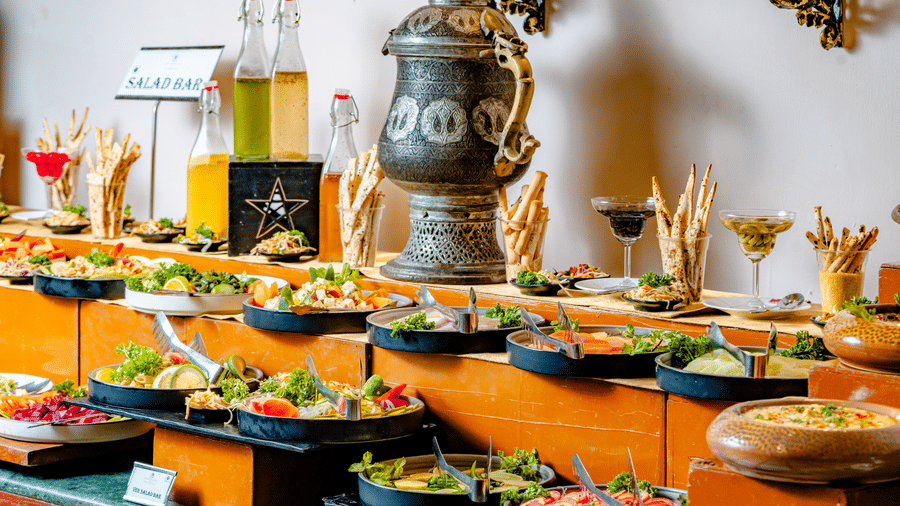 A tiered buffet display at Marble Arch, found at Noor-Us-Sabah Palace, Bhopal, featuring various cold salads, appetizers, and breadsticks.