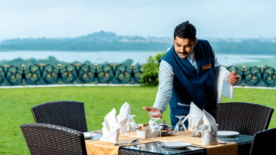 A staff member at Noor-Us-Sabah Palace, Bhopal, placing the glassware on the dining table overlooking the lush green lawn and the lake at the Marble Arch.