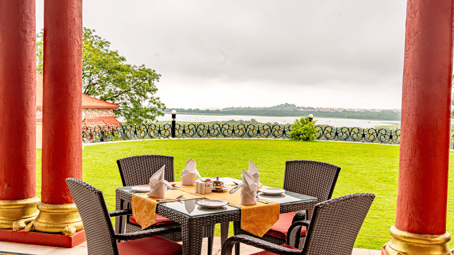 A dining table with orange table cloth spread over it in the outdoor space of the Marble Arch restaurant with expansive lawn and lake views at Noor-Us-Sabah Palace, Bhopal.