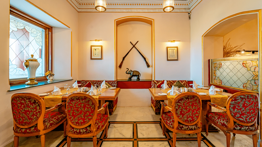 2 dining tables in a bright spaces of the Marble Arch restaurant at the Noor-Us-Sabah Palace, Bhopal, along with 2 rifles wall-mounted as a showpiece.