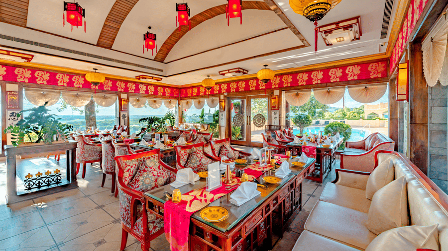 A wide-angle shot of the vibrant indoor dining hall at Ming Dynasty, located at Noor-Us-Sabah Palace, Bhopal, decorated with traditional red and yellow lanterns and elegant silk-patterned seating.