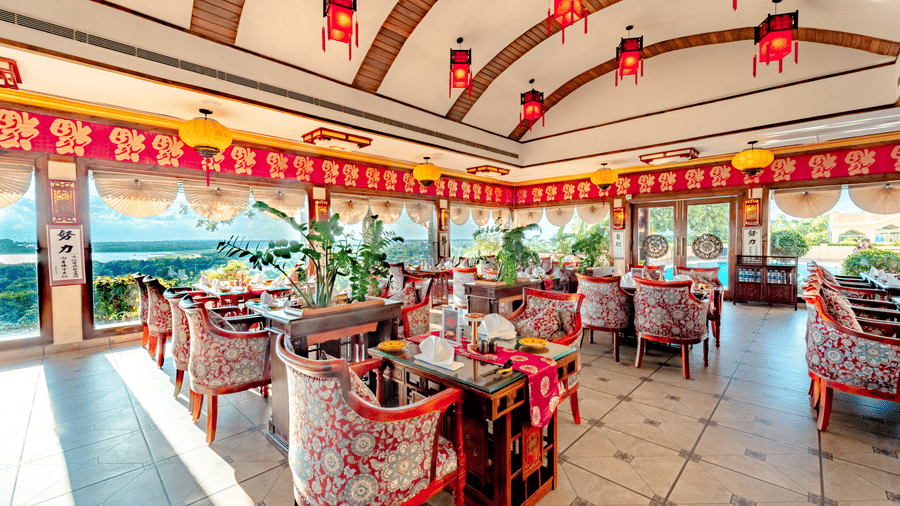 Interior of Ming Dynasty, part of the Noor-Us-Sabah Palace, Bhopal, featuring ornate red lanterns, patterned chairs, and large windows overlooking the grounds.