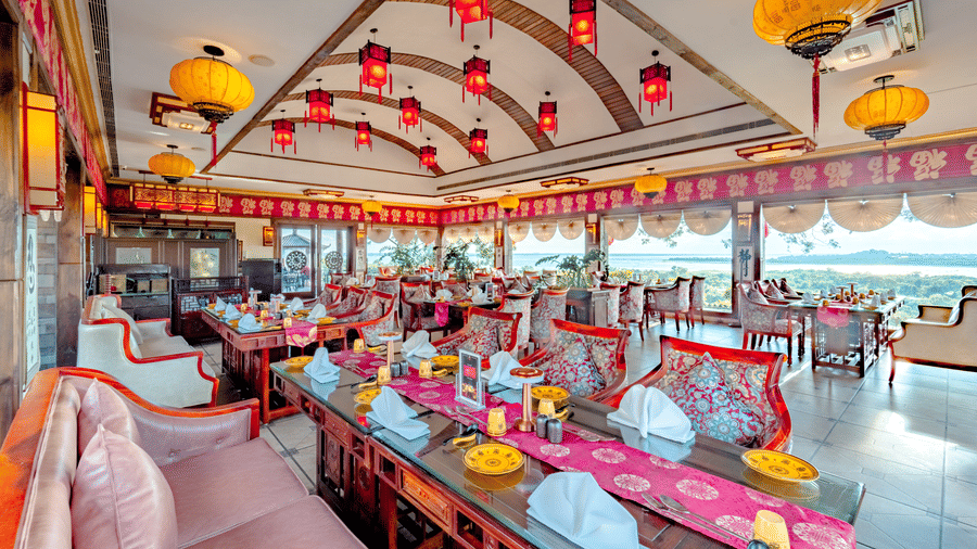The vibrant indoor dining hall at Ming Dynasty, found at Noor-Us-Sabah Palace, Bhopal, decorated with traditional red and yellow lanterns and elegant silk-patterned seating.
