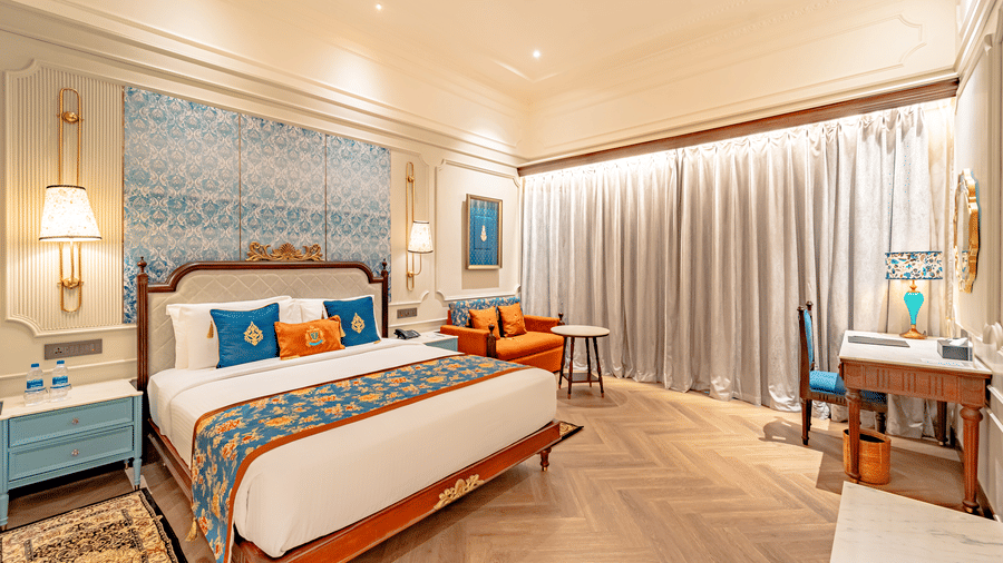 The elegant Premium Club Room at Noor-Us-Sabah Palace, Bhopal, highlighting the bed's patterned headboard, bedside lamps, and a dedicated workspace by the window.