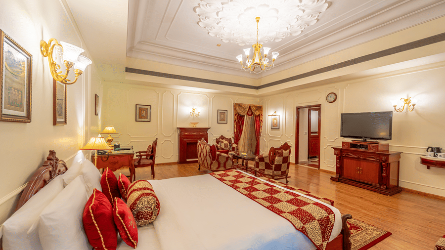 An overhead shot of the Presidential Suite at Noor-Us-Sabah Palace, showcasing the plush bedding, a dedicated vanity or work desk, and a wall-mounted television, all bathed in warm, soft lighting that highlights the room's regal decor.