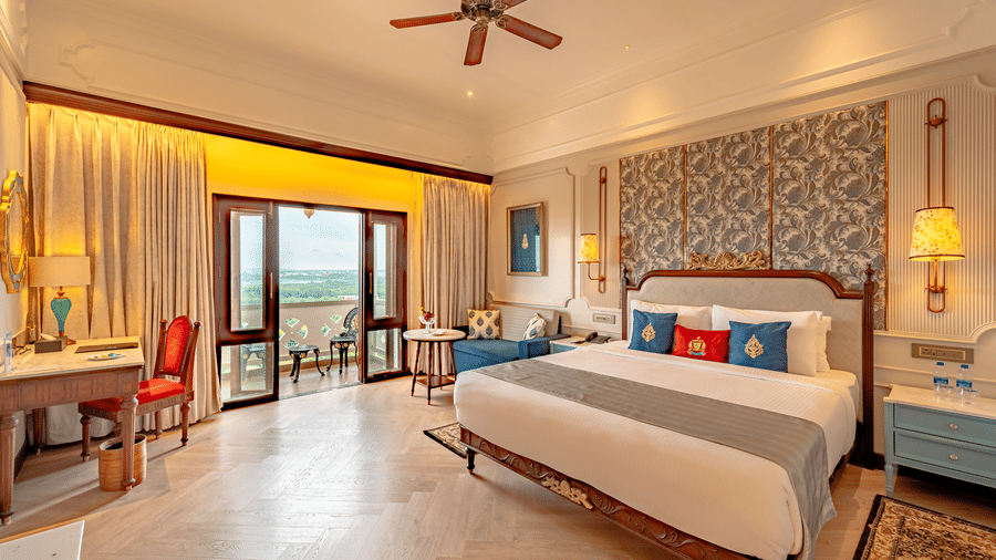 A wide-angle shot of the brightly lit Royal Club Room featuring a plush king size bed, along with the balcony windows opening to the beautiful green views of the forest.