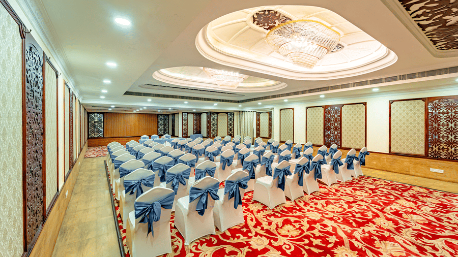 A wide-angle shot of a brightly lit Viceroy banquet hall at the Noor-Us-Sabah Palace, Bhopal, with all the chairs placed on the red carpeted section of the hall.