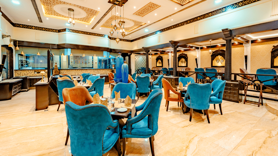 A wide-angle shot of the dining hall at Za-aiqa, located within Noor-Us-Sabah Palace, Bhopal, featuring elegant teal and orange armchairs.
