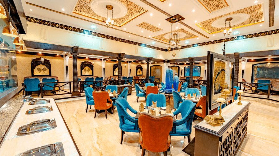 The interior of Za-aiqa at Noor-Us-Sabah Palace, Bhopal, showing the dining area from a different angle, highlighting the buffet service counter and the ornate ceiling design.