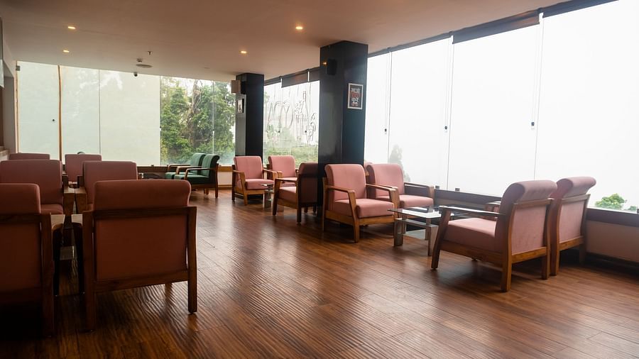 A wide shot of a spacious room with polished wooden floors, large windows, armchairs, and small tables at Orsino Spa Resort.