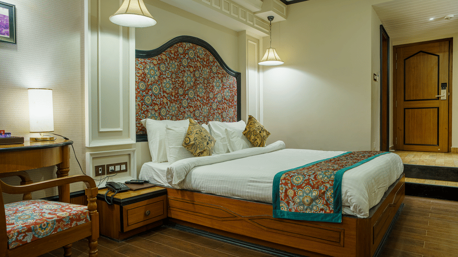 A room at Orsino Spa Resort, Darjeeling, with a large bed, decorative headboard, bedside tables with lamps, and a patterned throw on the bed.