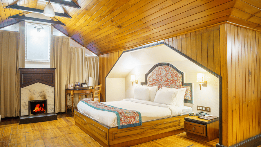 A room at Orsino Spa Resort, Darjeeling, with a wooden ceiling, a bed with a patterned throw, and a small fireplace.