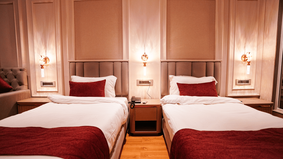 A room at Orsino Spa Resort with two single beds, each dressed in white linen with a red bed runner, and wall-mounted lights.