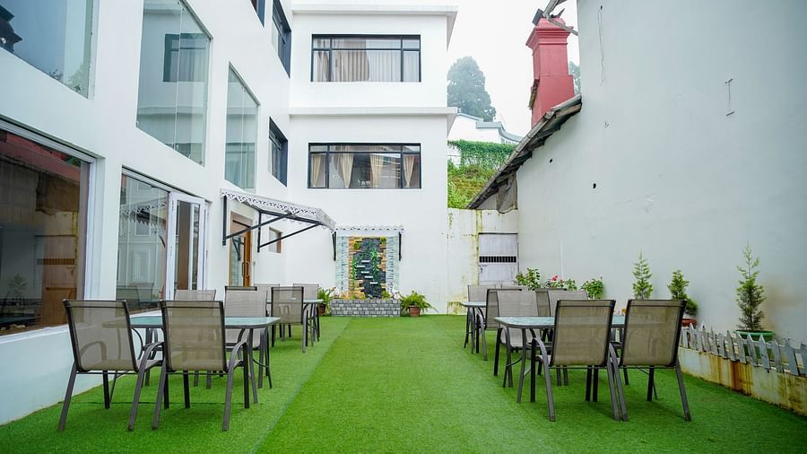 An outdoor seating area at Orsino Spa Resort with tables and chairs on a vibrant green lawn, framed by white buildings.