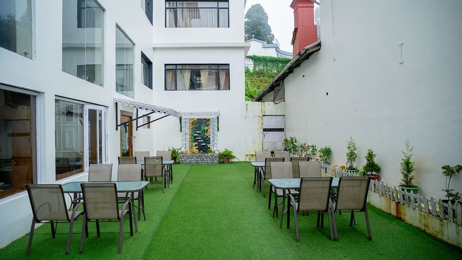 An outdoor seating area at Orsino Spa Resort with tables and chairs on a vibrant green lawn, framed by white buildings.