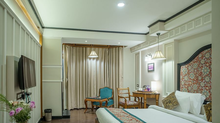A room at Orsino Spa Resort with a bed, a television, and a small sitting area, with large windows and light-coloured decor.