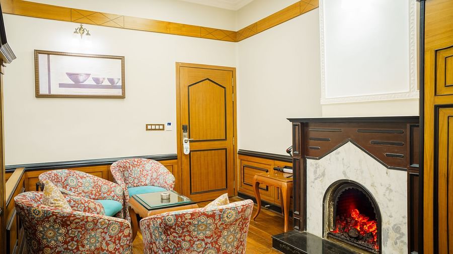 A seating area at Orsino Spa Resort with patterned armchairs and a sofa, a fireplace with a lit fire, and wooden wall panelling.