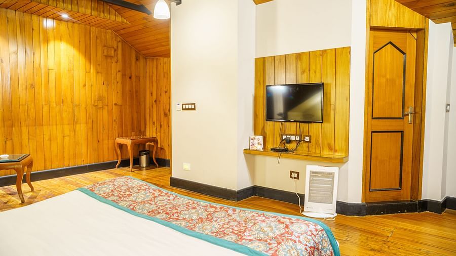 A room with a bed featuring a colourful patterned throw, wooden panelling on the walls, and a television mounted on the wall at Orsino Spa Resort.