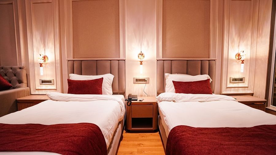 A room at Orsino Spa Resort with two single beds, each dressed in white linen with a red bed runner, and wall-mounted lights.