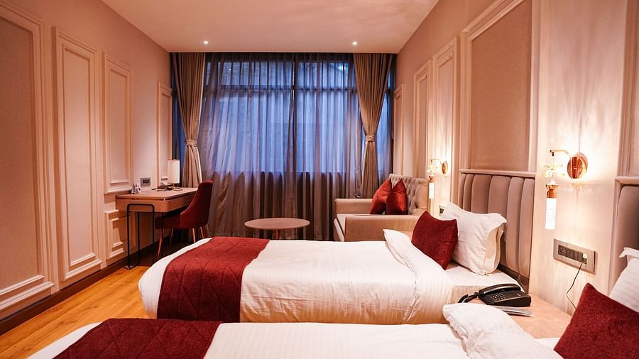 A room at Orsino Spa Resort with two beds, each made up with white linen and a red bed runner, set against a dark feature wall with curtains.