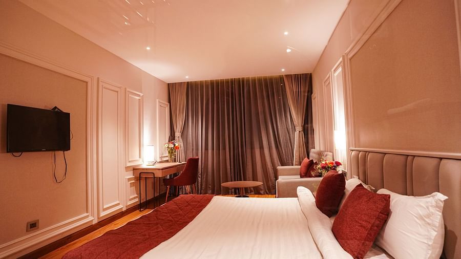 A room at Orsino Spa Resort with a large bed dressed in white linen and a red bed runner, with curtains and warm lighting.