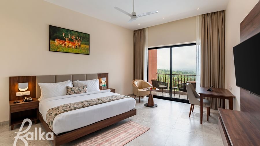 A spacious bedroom at Osian Valley Resort & Spa with a large bed, a desk and chair, a wall-mounted television, and a balcony with a scenic view.