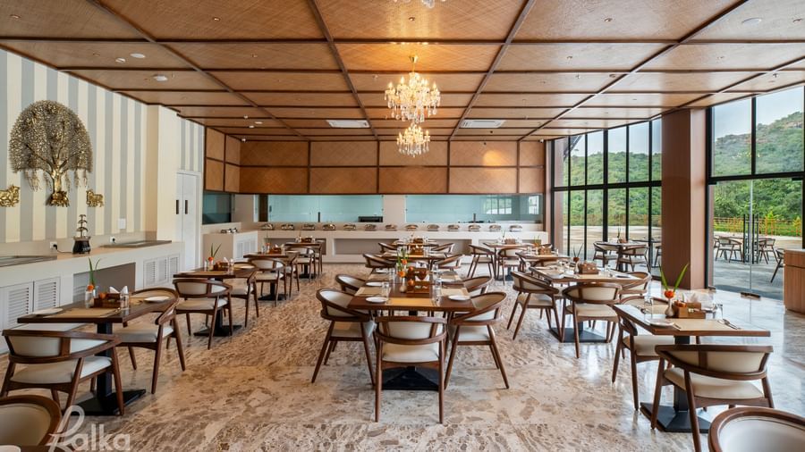 A well-lit restaurant interior at Osian Valley Resort & Spa with multiple square wooden tables and chairs arranged on a patterned floor. 