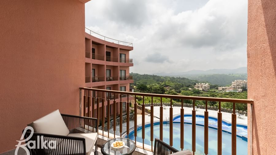A balcony at Osian Valley Resort & Spa, furnished with 2 chairs, overlooking a swimming pool and a valley with green hills.